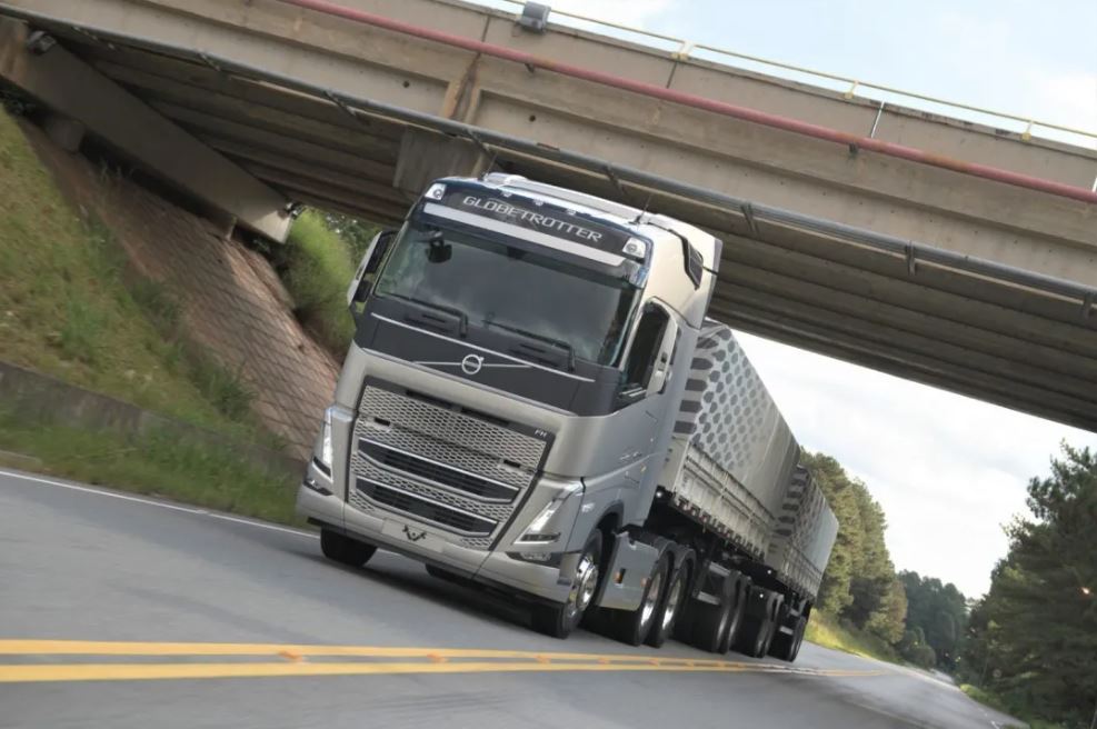 Imagem mostra um caminhão volvo cinza na estrada onde é possível ver a estrada e um viaduto