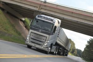 Imagem mostra um caminhão volvo cinza na estrada onde é possível ver a estrada e um viaduto